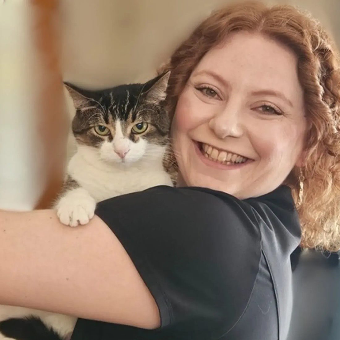 Smiling woman with curly hair holding a tabby cat