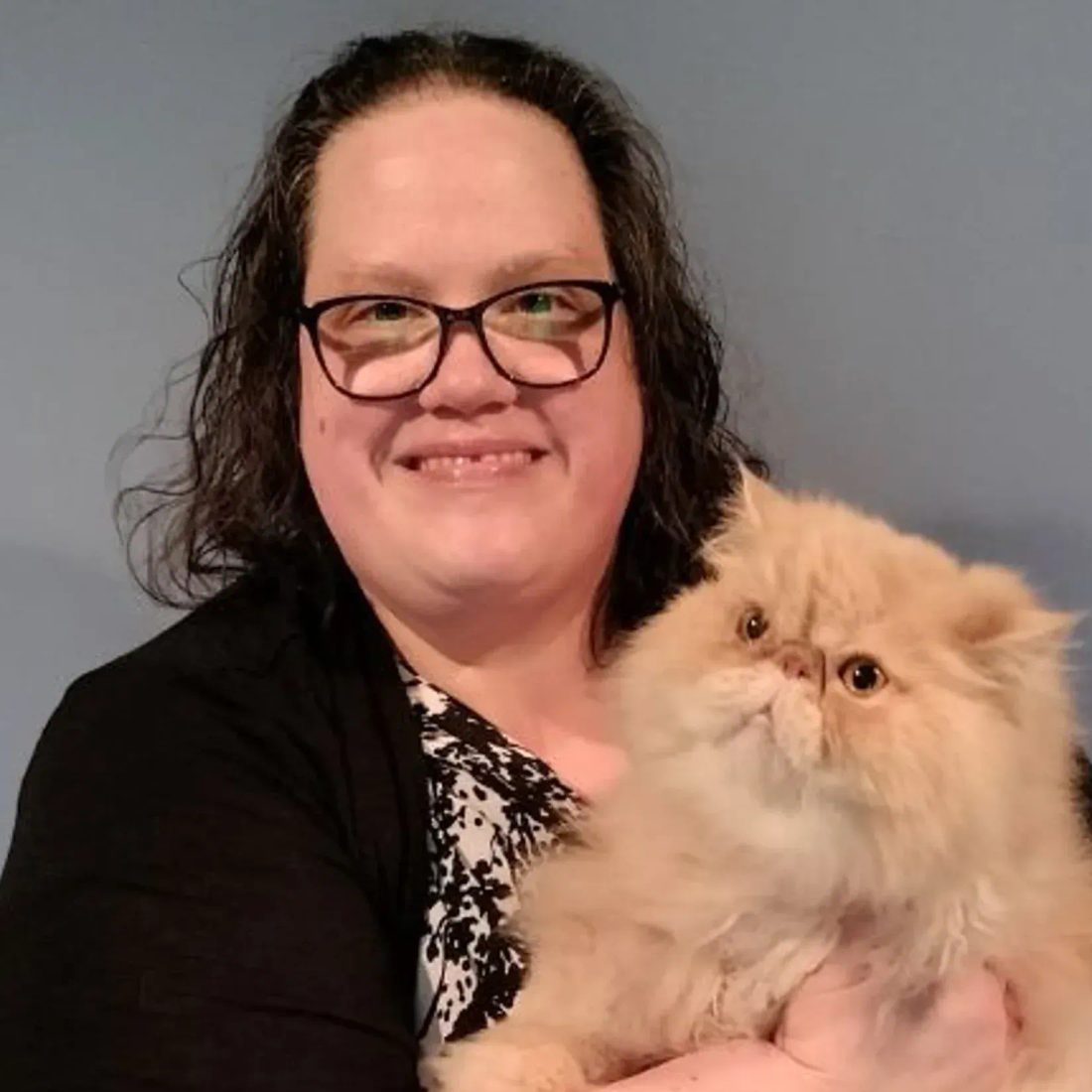 Smiling woman with glasses holding a fluffy orange cat