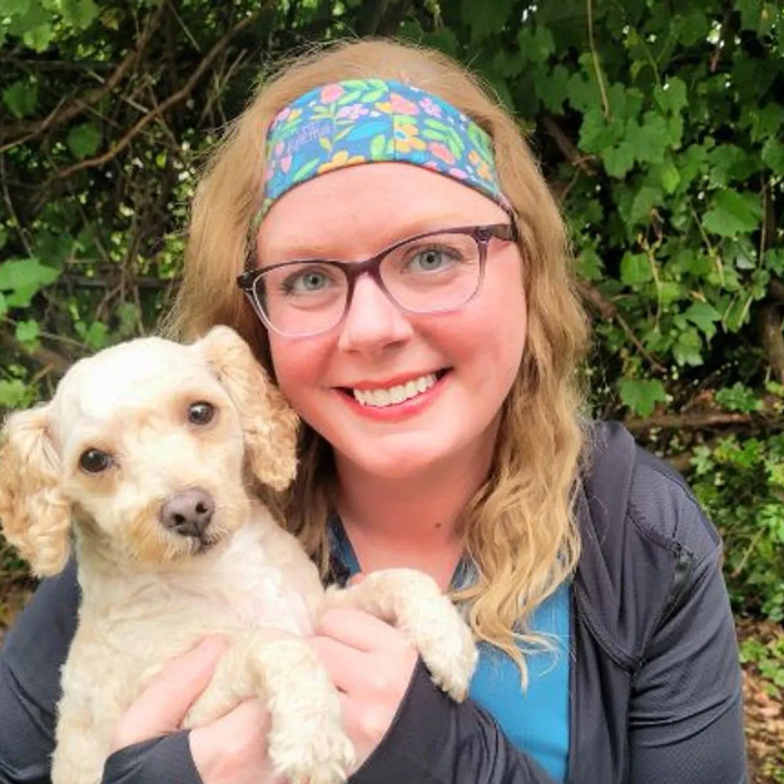 Woman with glasses and headband holding a small white dog outdoors